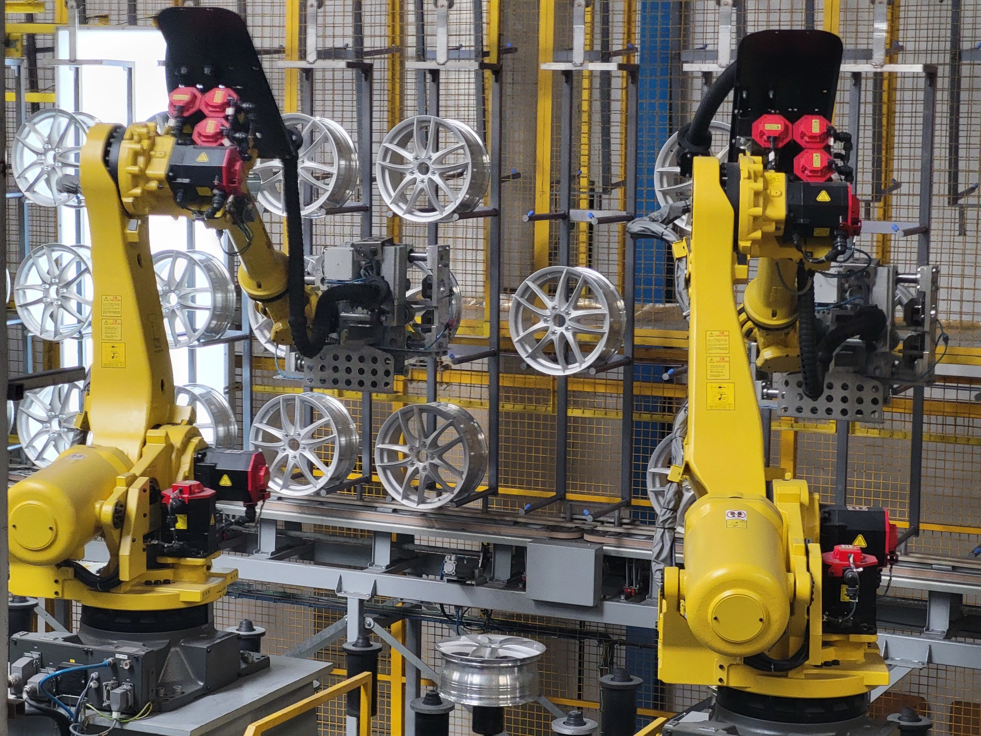 Roboty przemysłowe z chwytakami produkcji Wikpol do automatycznego przewieszania felg w linii produkcyjnej.